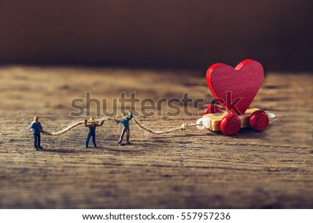 Miniature worker try to tow red heart shape of wooden toy train on grunge wooden floor,Image for team building or love valentine day concept.