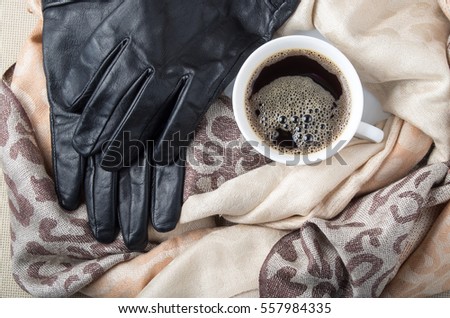 Top view of a white cup of coffee in the folds of the women's shawls and black leather gloves
