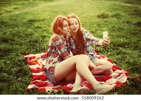 Two young hipster girls having fun on the picnic, making selfie on a smartphone