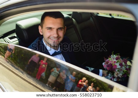 handsome and happy groom with flowers sitting in the car and smiling