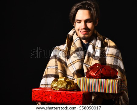 handsome bearded smiling man in checkered plaid holding colorful presents or gifts on black studio background