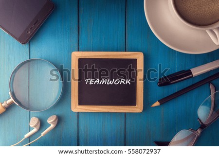 Top view of TEAMWORK written on the chalkboard,business concept.chalkboard,smart phone,cup,magnifier glass,glasses pen on wooden desk.