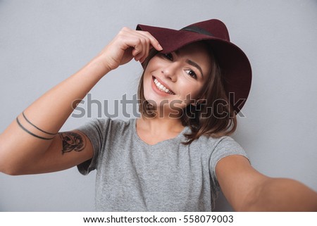 Portrait of a laughing woman in hat and scarf making selfie photo over gray background