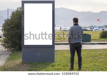 Man looking at empty billboard standing in outdoor urban park with grass and blue sky. Mock up, 