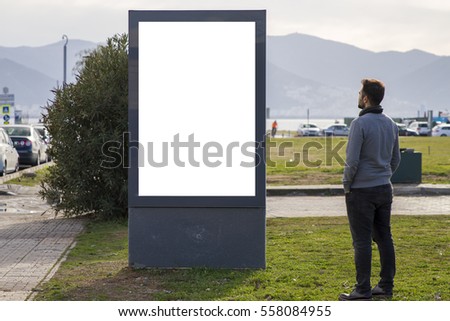 Man looking at empty billboard standing in outdoor urban park with grass and blue sky. Mock up, 