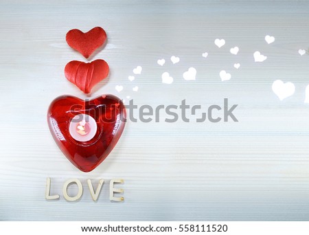 Two small heart and candlestick candle in form of big red heart on light wooden texture, word "love" volumetric letters.  Greeting card design concept background for lovers, Valentine's Day, birthday.