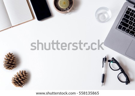 White office desk table with laptop, smartphone, pen, open diary, cactus, pinecones and glass. Top view with copy space, flat lay.