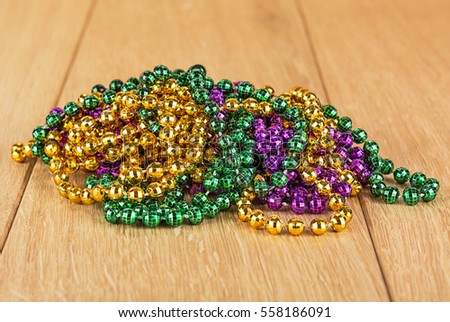Green, purple, and gold mardi gras beads isolated on wood