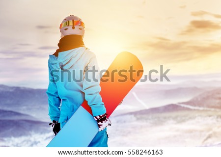 Girl snowboarder stands with snowboard on mountain's top on sunrise backdrop. Sheregesh ski resort