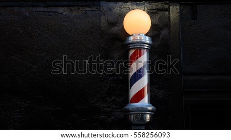 Barbershop pole against black brick wall. Royalty-Free Stock Photo #558256093