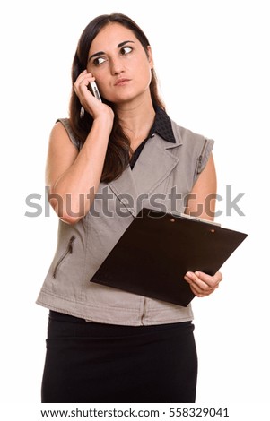 Studio shot of beautiful businesswoman talking on mobile phone while holding clipboard isolated against white background