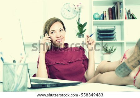 young smiling female employee answering on phone and sitting relaxed with legs on working table at office 