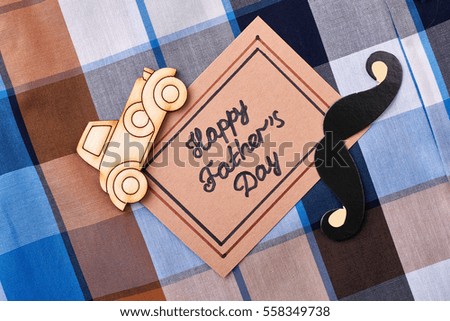 Greeting card on gingham background. Props mustache and wooden car. Handmade surprise for daddy.