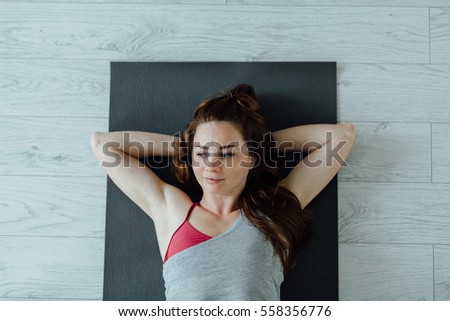 Top view of attractive woman  with bright foxy hair wearing gray and vinous sportswear  relaxing on yoga mat l in fitness studio. Healthy life concept 