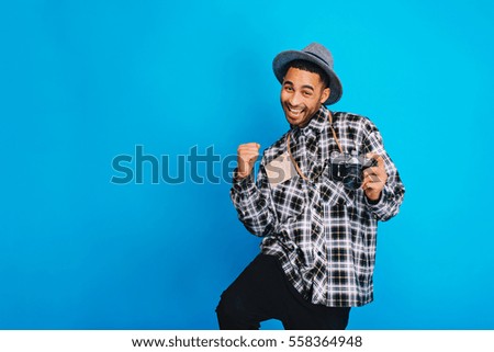 Excited joyful young handsome man expressing positive emotions on blue background. Traveling, tourism, camera, map, cheerful mood, happiness, positivity, journey, smiling. Place for text
