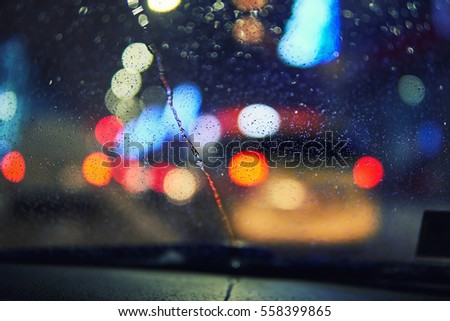 Blurred winter picture. Blurred background with the city lights at night. Riding the machine by road. Snowfall in the city. Car windshield wipers clean the snow window
                             