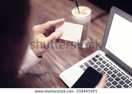 Close-up of man hands holding business card, working on laptop in cafe with internet, drinking latte