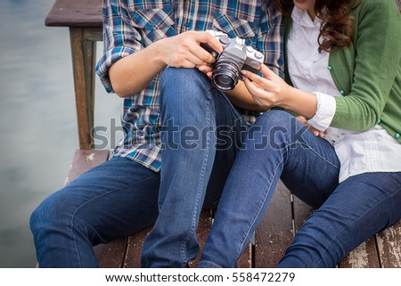 Young men and young women Couple together sitting on bench waterfront port in the park. Handle vintage camera.