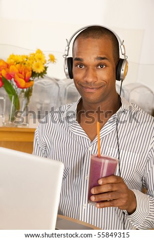 Man is holding a smoothie while sitting at the computer and smiling at the camera.  Vertical shot.
