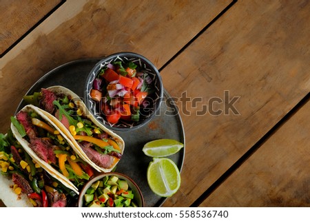 Tacos with ingredients meat and vegetables on the plate on a dark brown wooden background, top view. Lots of space for text and design.