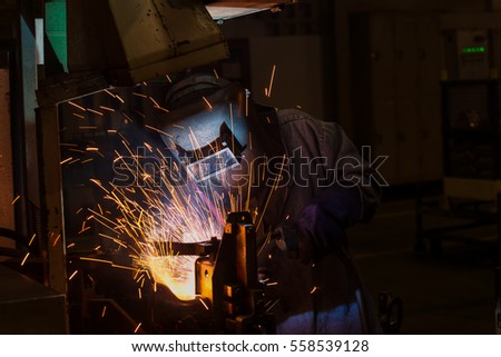 Industrial worker is welding automotive part in car factory with protective mask

