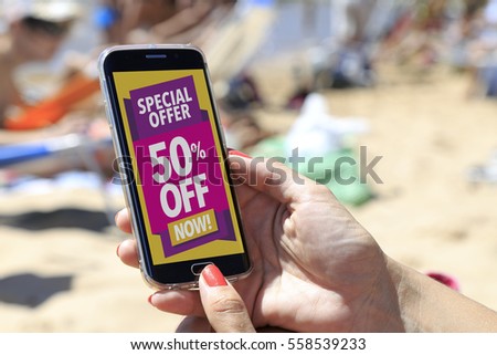 Woman at the beach with a smartphone with a 50% discount advertising on the screen.