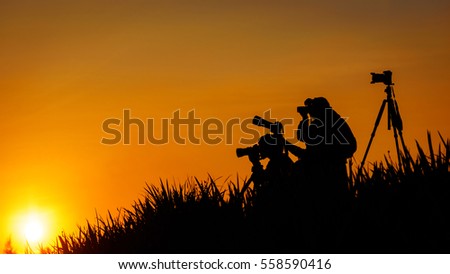 Silhouette of photographers group on grass hill in sunset evening 