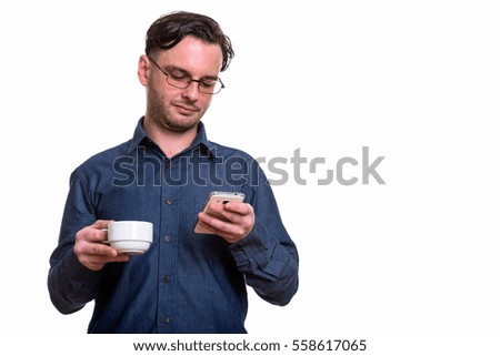 Studio shot of formal young man using mobile phone while holding coffee cup isolated against white background
