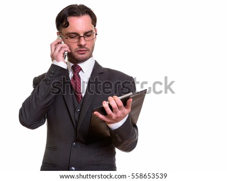Studio shot of young businessman talking on mobile phone while reading on clipboard isolated against white background