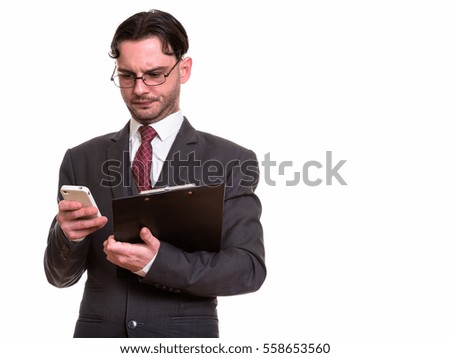 Studio shot of young businessman using mobile phone while holding clipboard isolated against white background