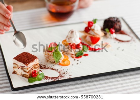 Tasting one cake from lots, close-up. Plate with five different sweet desserts, hand taking one. Degustation, choosing dessert for party or wedding, gastronomy, event organization concept Royalty-Free Stock Photo #558700231