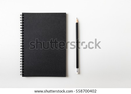 Top view of closed black cover notebook with pencil on white desk background