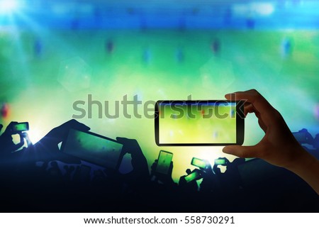 Silhouette of hands using smart phone to take pictures and videos at live football game