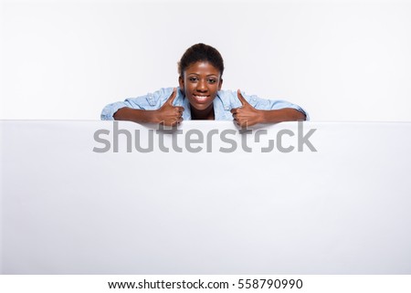 smiling and cheerfull black woman leaning on an white empty board showing confidence and joy