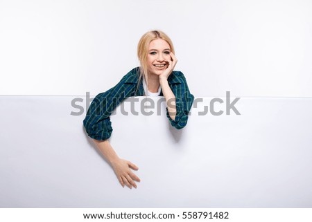 young beautiful blonde woman casual dressed leaning over an white empty panel with free space isolated on white