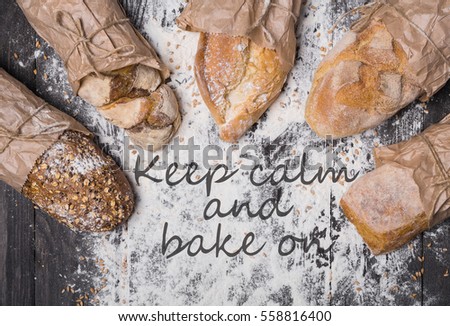 Cooking concept background. Keep calm and bake text, different bread sorts, wrapped in craft paper top view with copy space in the middle on wooden table, sprinkled with flour. Soft toning