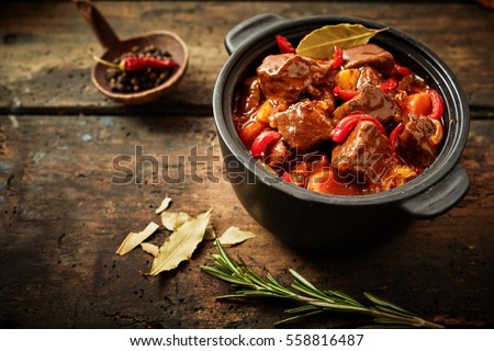 Pot of hungarian goulash on rustic wood background with chili peppers and laurel and copy space Royalty-Free Stock Photo #558816487