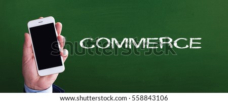 Smart phone in hand front of blackboard and written COMMERCE