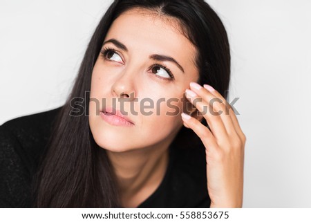 Close up portrait of brunette pretty woman with headache touching her face, look up. Beautiful woman stressed and worry in black sweater on light grey background. Health care and medicine.