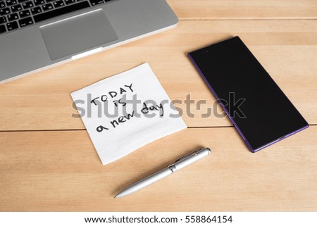 Laptop with paper cup, smartphone, pen and napkin with message on wooden desk. Morning workspace in office