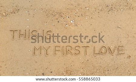 Handwriting words "THIS IS MY FIRST LOVE" on sand of beach