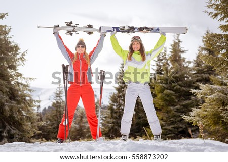Beautiful young woman friends enjoying in ski vacations. They are standing with skis and having fun.