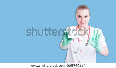 Joyful female medic  showing visit card and doing ok gesture on blue background with copyspace