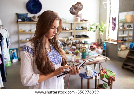 Teenage boutique assistant  using tablet computer in shop Royalty-Free Stock Photo #558976039