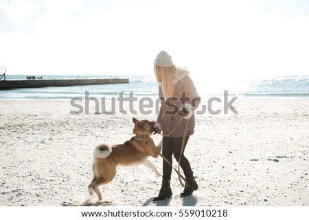 Picture of beautiful young girl walks in winter beach with dog on a leash.