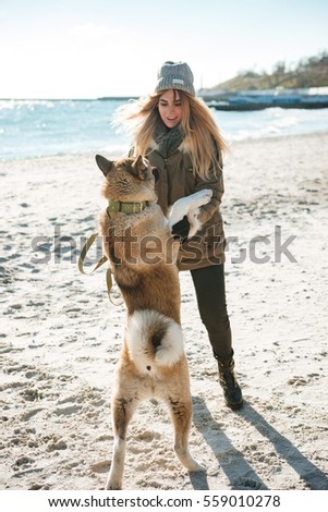 Picture of young playful lady walks in winter beach with dog on a leash.
