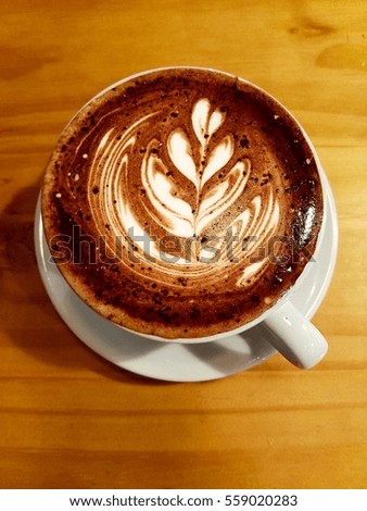 white coffee cup on the wooden surface filled with the coffee art picture of the plant