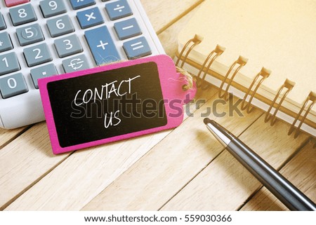 Notebook, pen, calculator and wooden tag written with CONTACT US on wooden background. Business Concept.