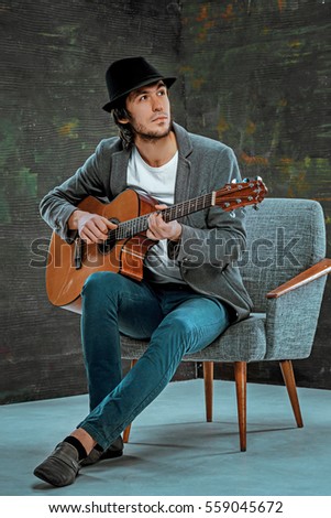 Cool guy with hat playing guitar on gray studio background