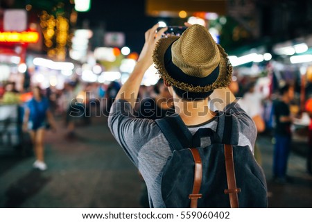 Young Asian traveler taking photo with mobile phone in Khaosan road at night in Bangkok, Thailand
